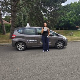 Ellie smiling proudly next to a car after passing her driving test, holding her certificate, celebrating her achievement with EXL Drivers.