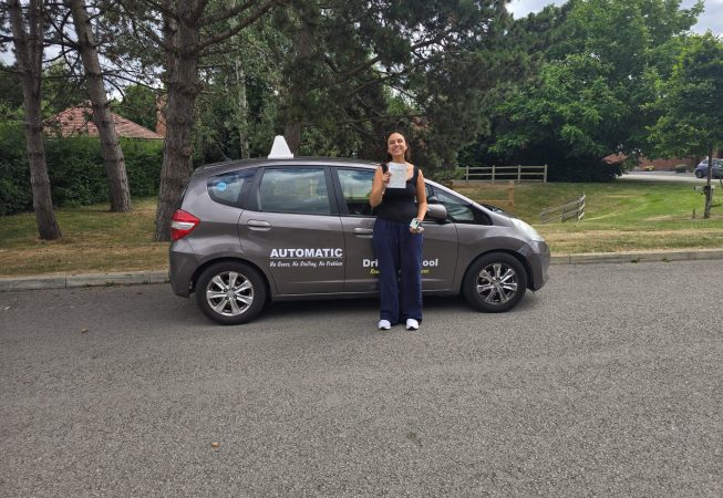 Ellie smiling proudly next to a car after passing her driving test, holding her certificate, celebrating her achievement with EXL Drivers.