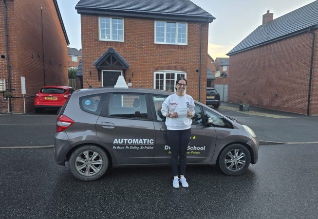 Sharon smiling and holding her driving test pass certificate after passing on her first attempt.